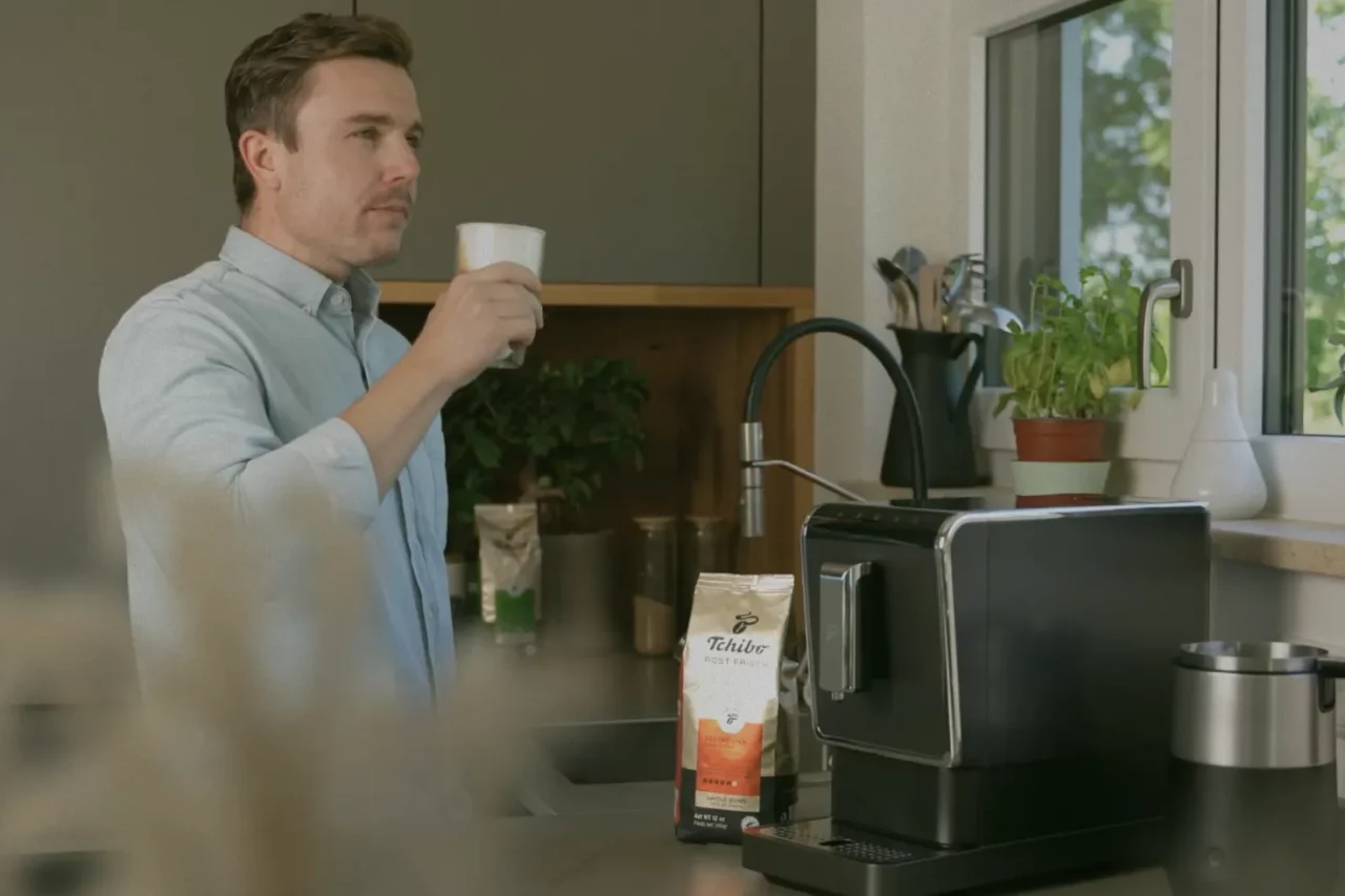Ausschnitt aus einem Video für die Röst Frisch Kaffeereihe für Tchibo US, Mann trinkt einen Schluck Latte Macchiatto in der Küche vorm Kaffeevollautomaten